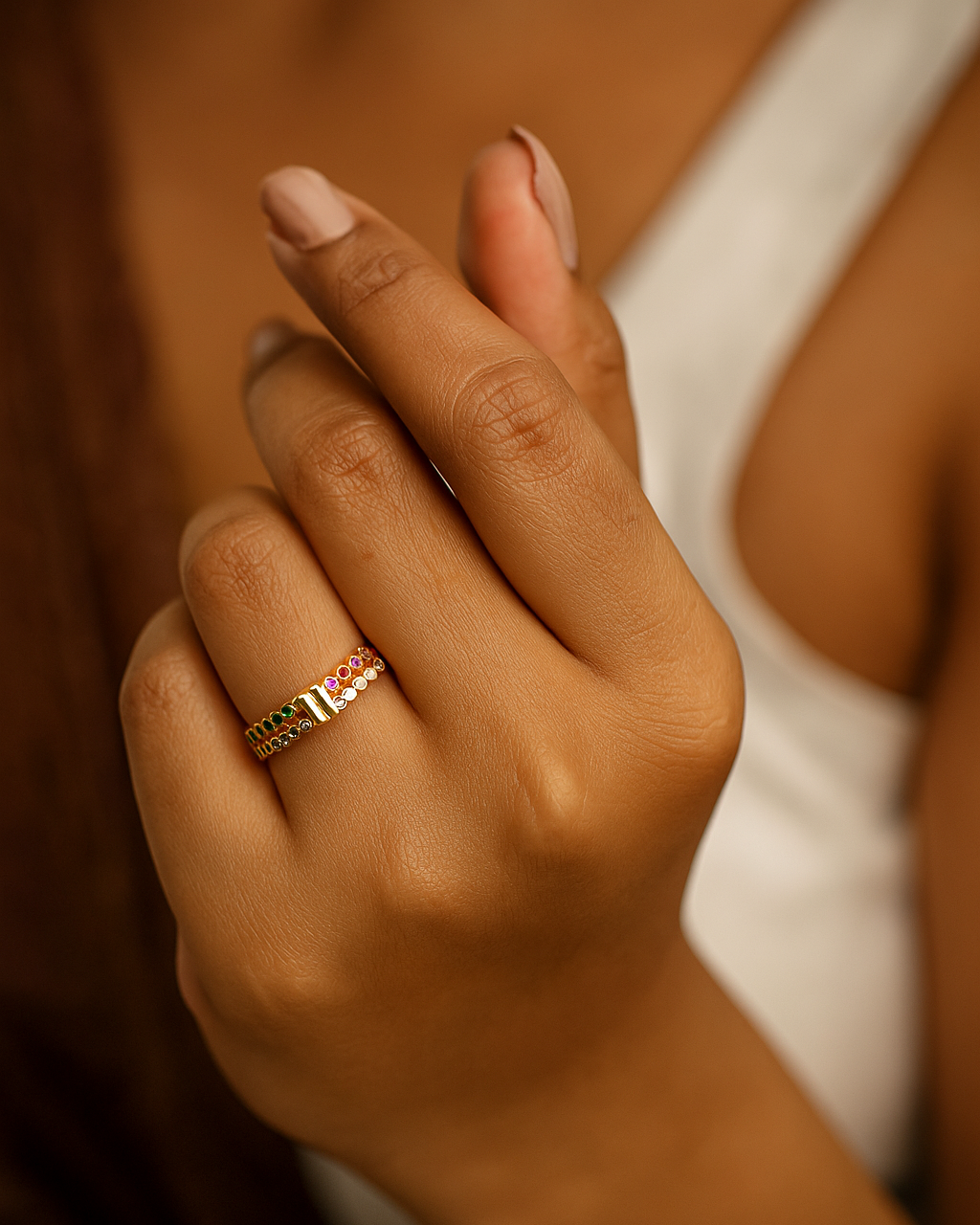 Close-up of a hand wearing a ring with a colorful gemstone against a blurred background