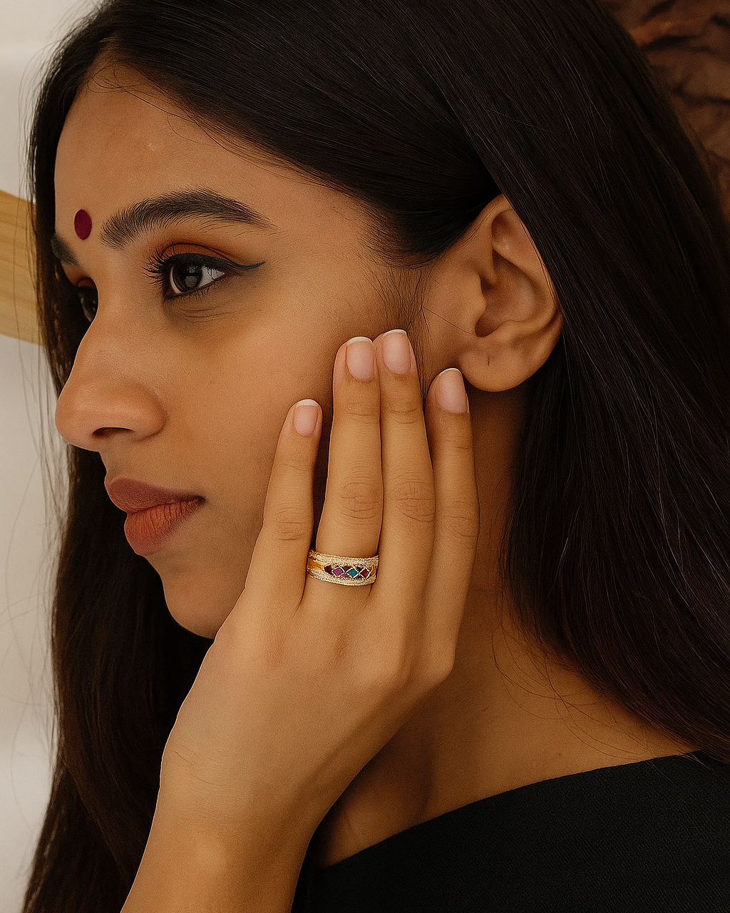 Woman with a ring on her finger touching her ear, wearing a black top.