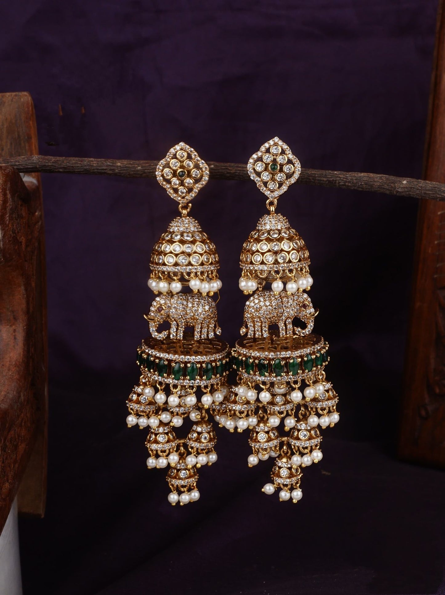 A pair of intricately designed traditional Jhumka earrings with gold-tone bases, white pearl encrusted domes, and green beads.