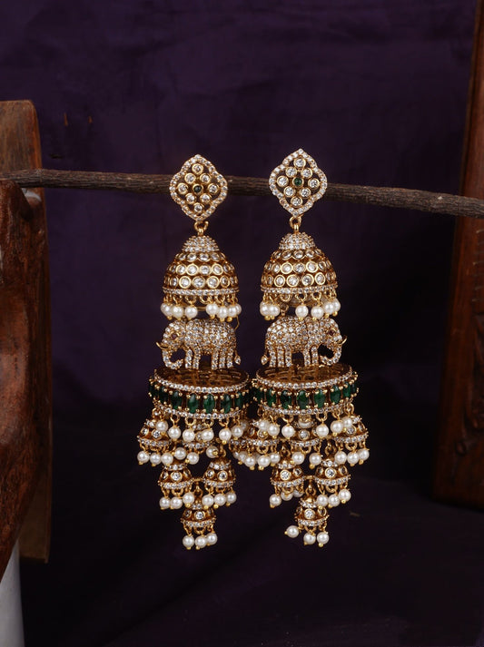 A pair of intricately designed traditional Jhumka earrings with gold-tone bases, white pearl encrusted domes, and green beads.
