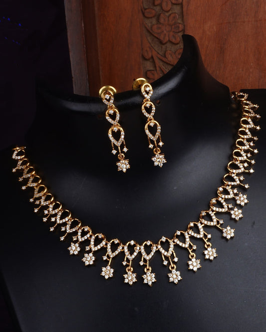 A gold-colored floral necklace and earrings set adorned with sparkling stones displayed on a mannequin.