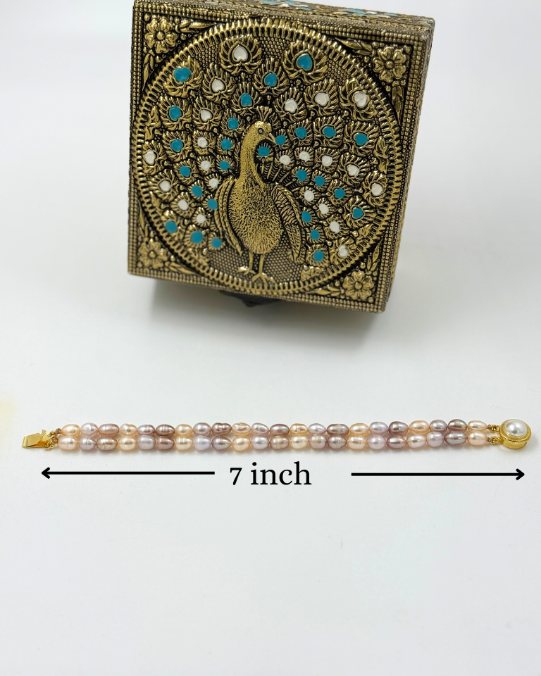 Decorative box with peacock design and a pearl bracelet on a white background