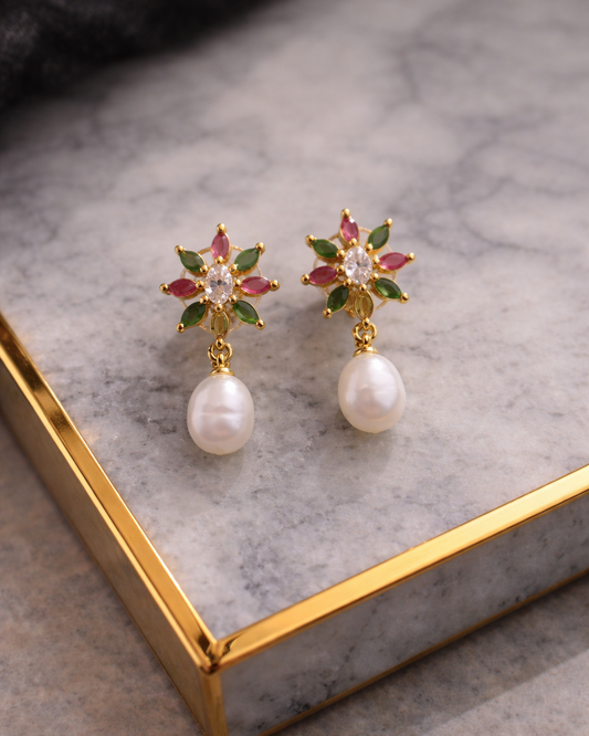 Pair of earrings with star-shaped top and pearl bottom on a marble surface