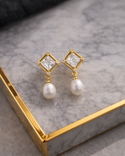 Gold earrings with clear gemstones and pearl drops on a marble surface