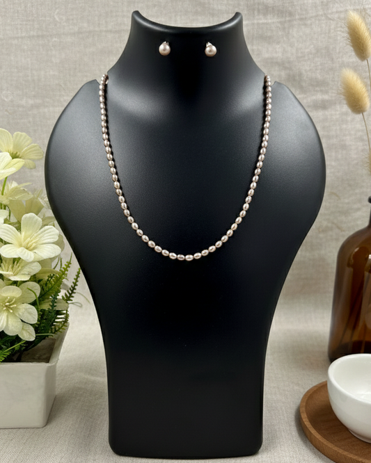Black jewelry stand with pearl necklace and earrings, placed on a light gray surface with decorative elements.