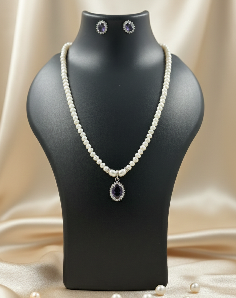 Pearl necklace with pendant on a black mannequin bust against a beige fabric background.