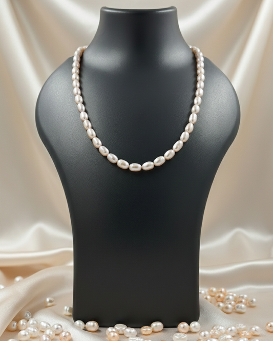 Pearl necklace on a black mannequin bust with scattered pearls on a beige fabric background