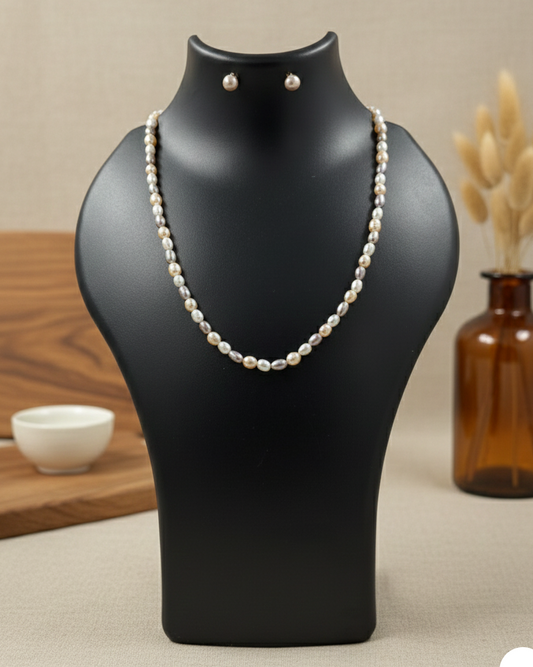 Pearl necklace and earrings on a black mannequin bust with a neutral background