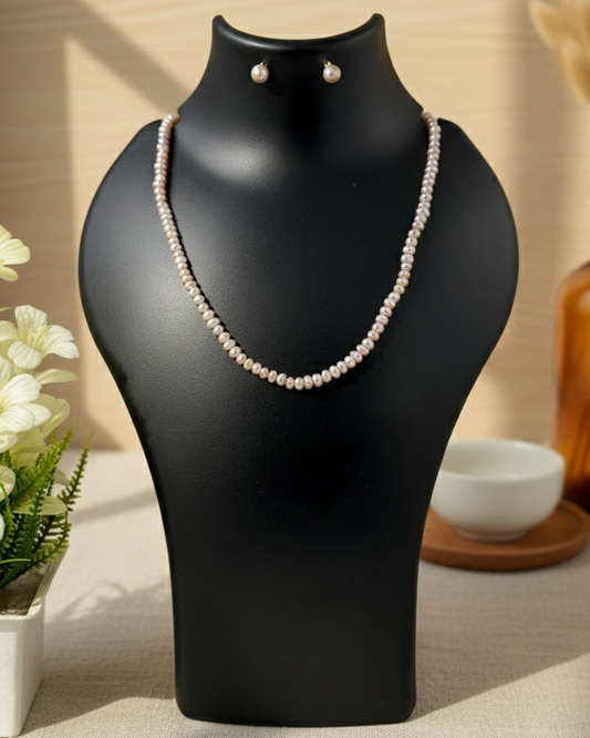 Pearl necklace and earrings on a black mannequin bust with a neutral background
