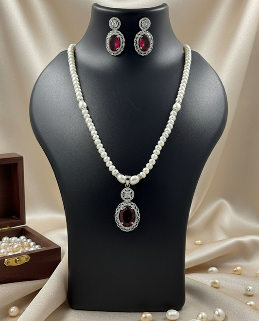 Pearl necklace and earrings on a black mannequin with a wooden box and scattered pearls on a beige fabric background.