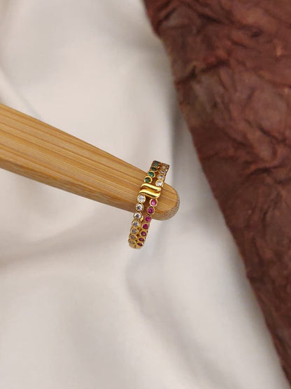 Gold ring with embedded gemstones on a wooden stand against a neutral background