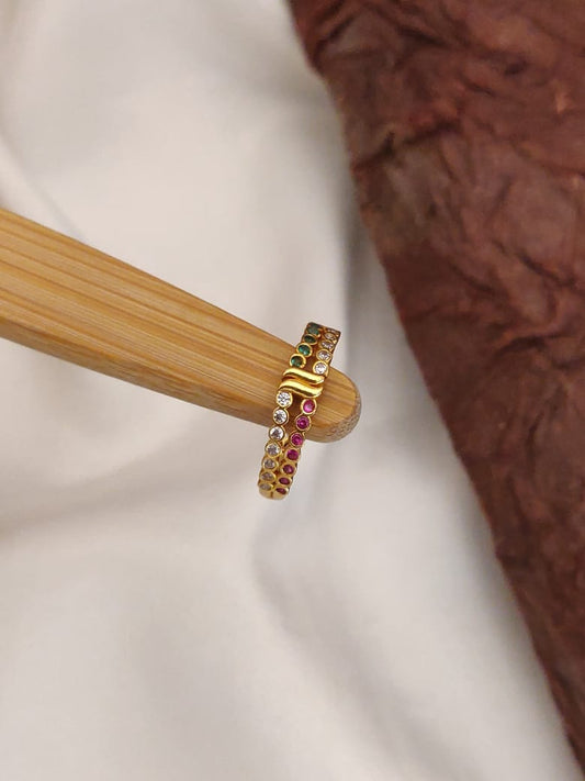 Gold ring with embedded gemstones on a wooden stand against a neutral background