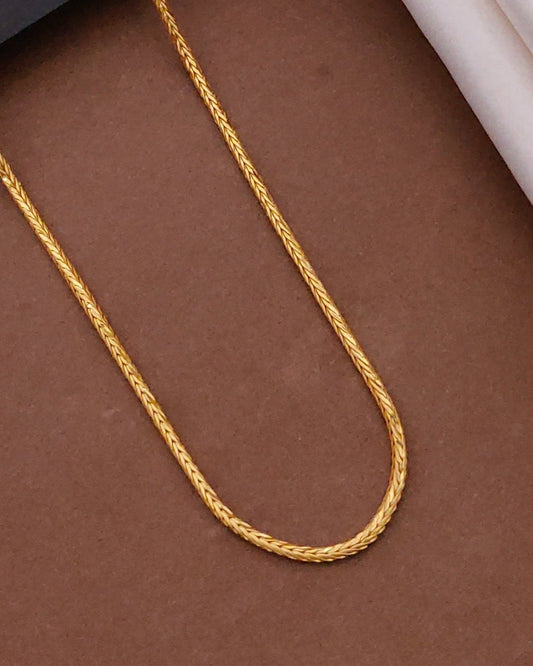 Gold chain on a brown surface with a black box and wooden frame in the background