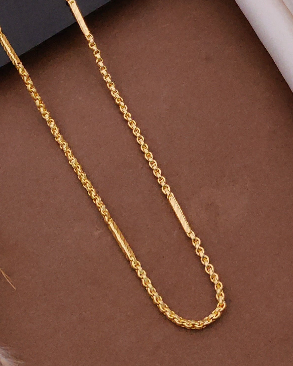 Gold chain on a brown surface with a black card and wooden frame in the background