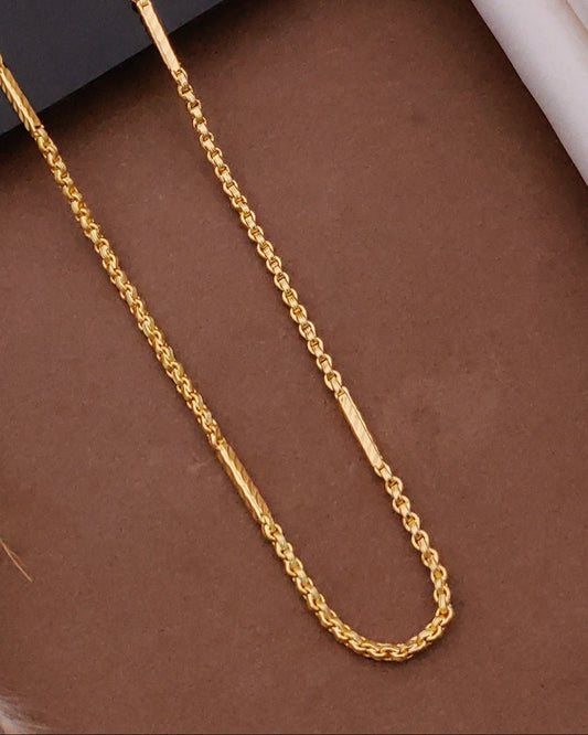 Gold chain on a brown surface with a black card and wooden frame in the background
