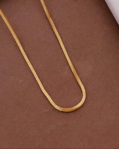 Gold chain on a brown surface with a black box and wooden frame in the background