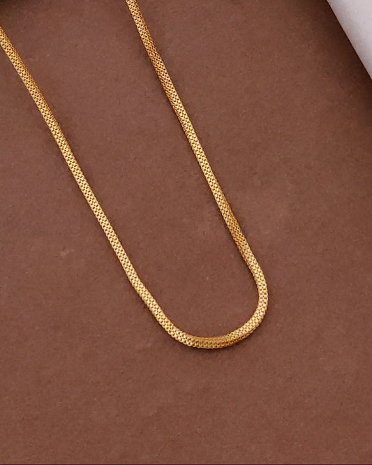 Gold chain on a brown surface with a black box and wooden frame in the background
