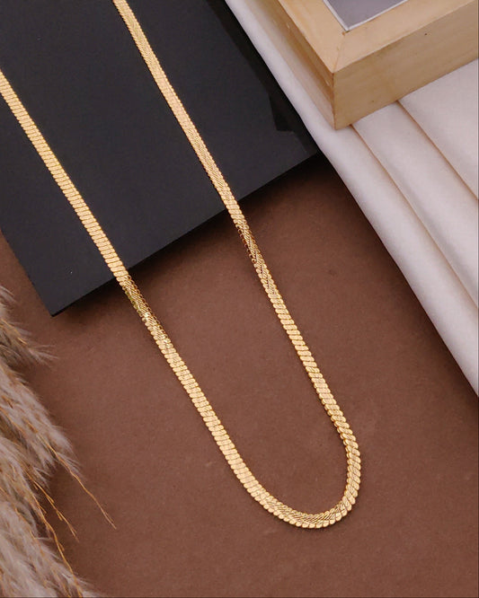Gold chain on a brown surface with a black box and wooden frame in the background