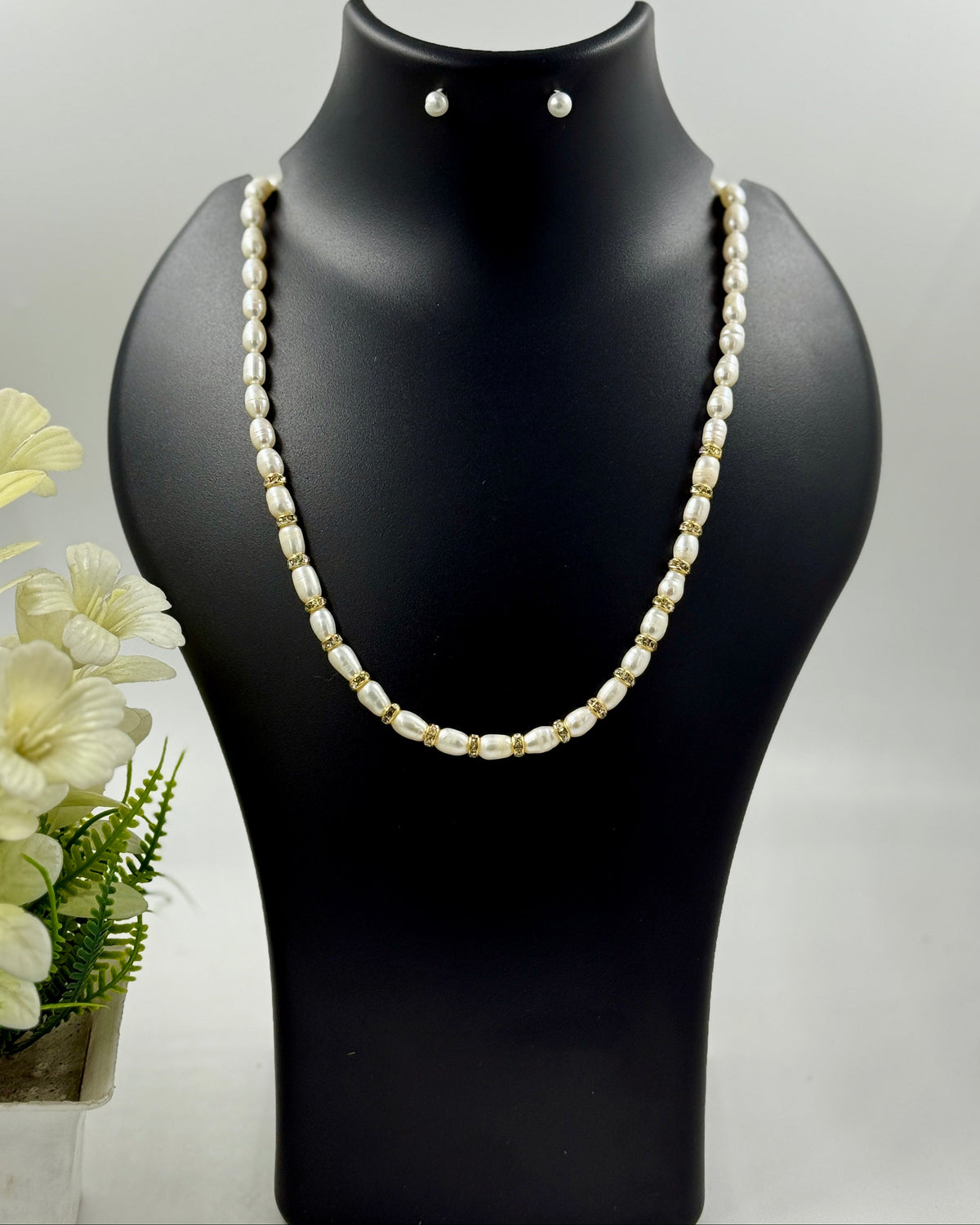 Pearl necklace on a black mannequin with earrings, against a light gray background.