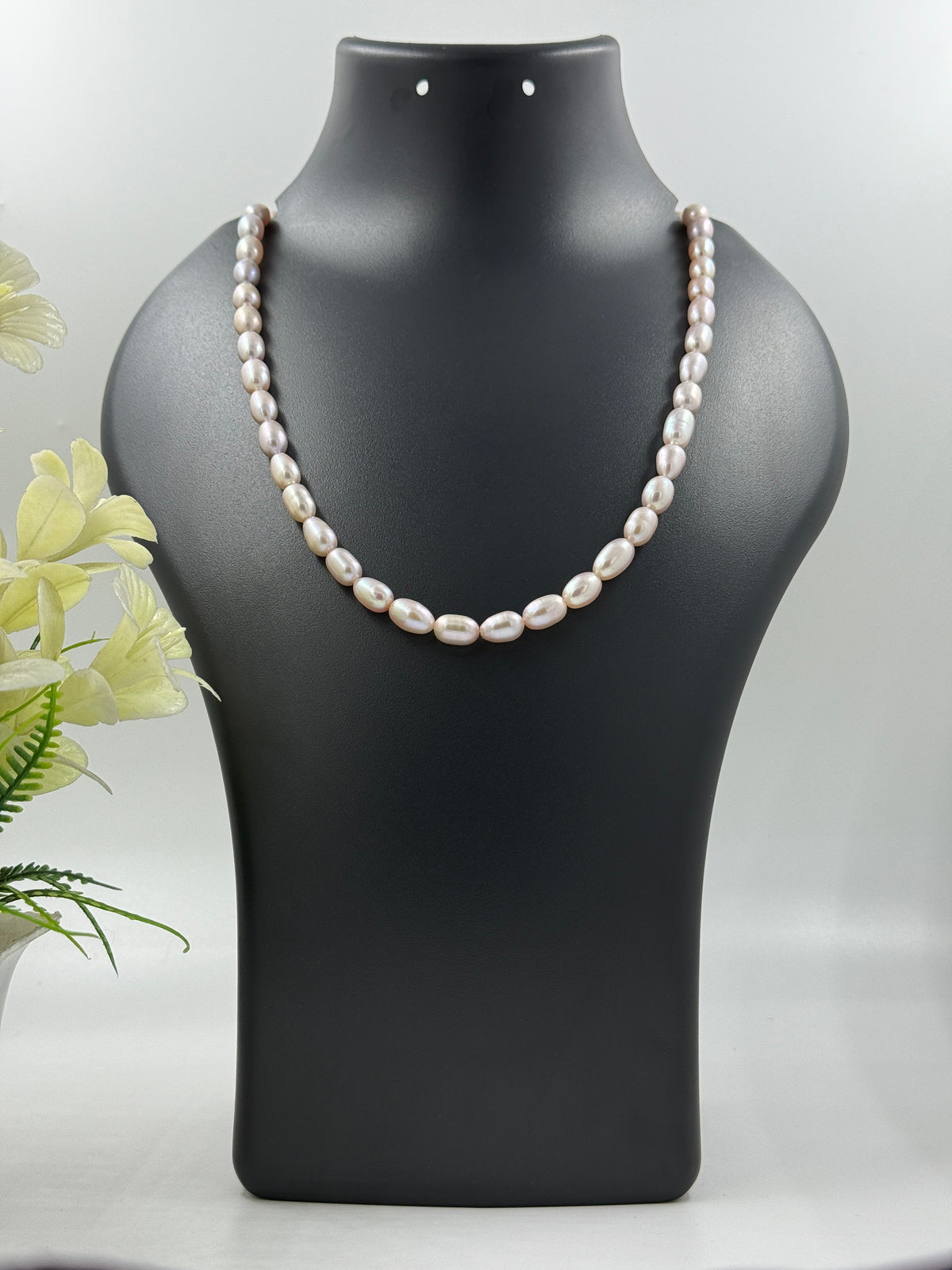 Pearl necklace on a black mannequin bust with a light gray background