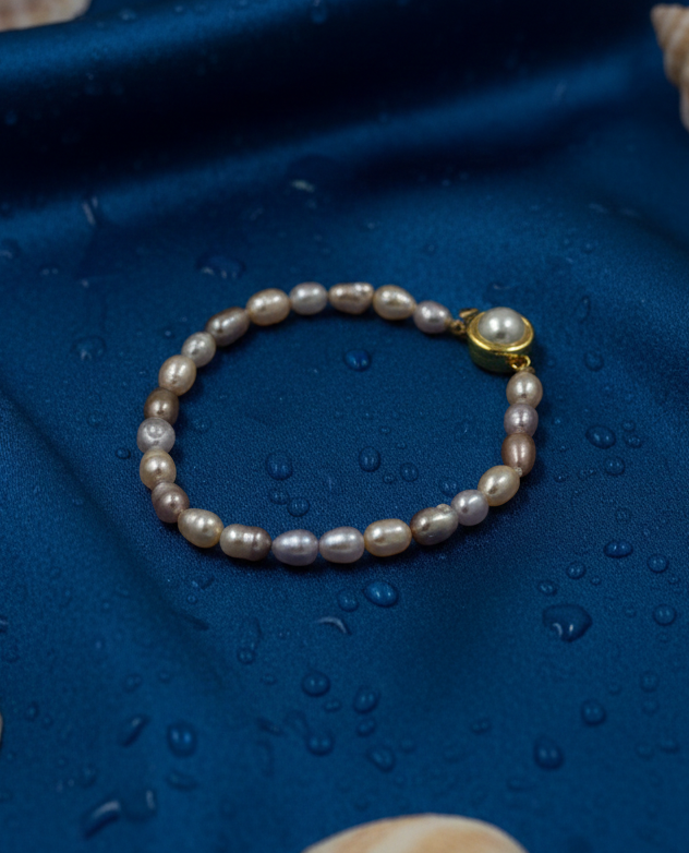Pearl bracelet with a gold clasp on a blue fabric background with shells.